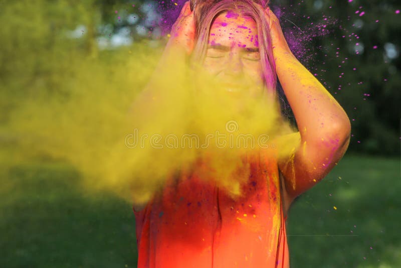 Closeup portrait of merry blonde girl having fun in a cloud of yellow and purple dry Holi paint. Closeup portrait of merry blonde woman having fun in a cloud of stock image